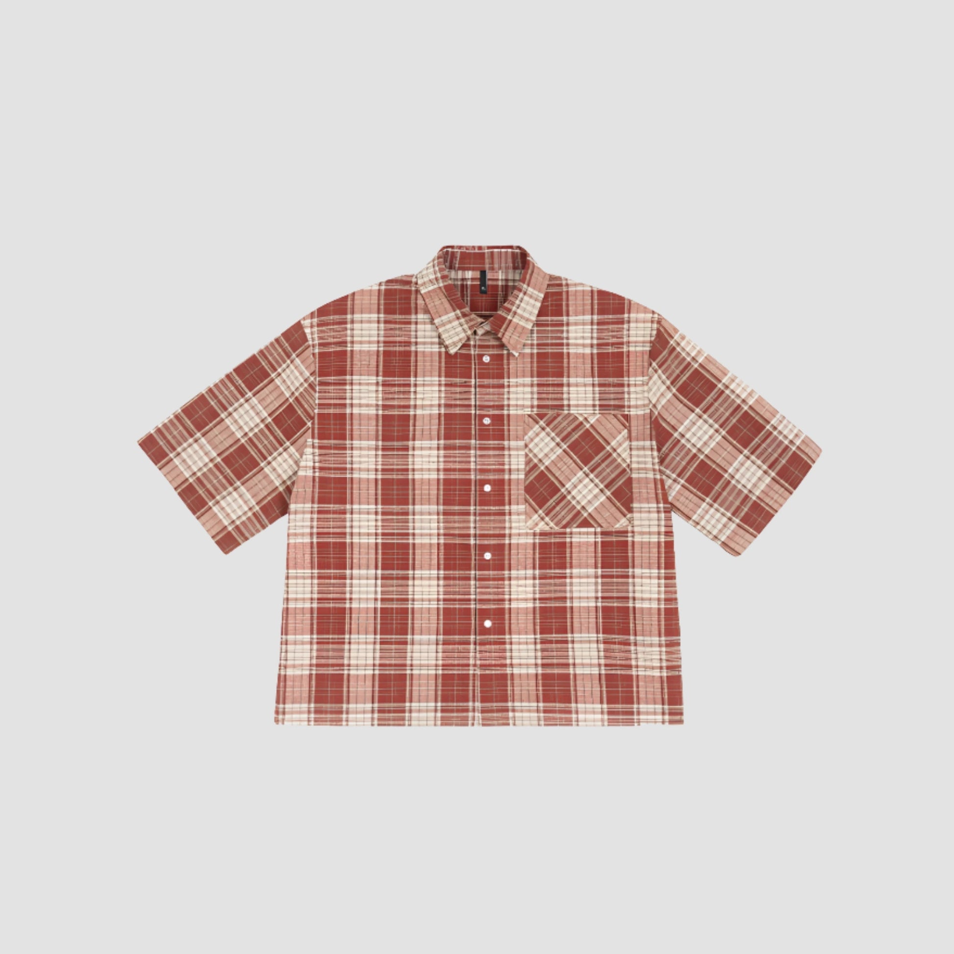 Chemise streetwear rouge, posée sur un fond gris, chemise à carreau et avec une poche sur le torse.